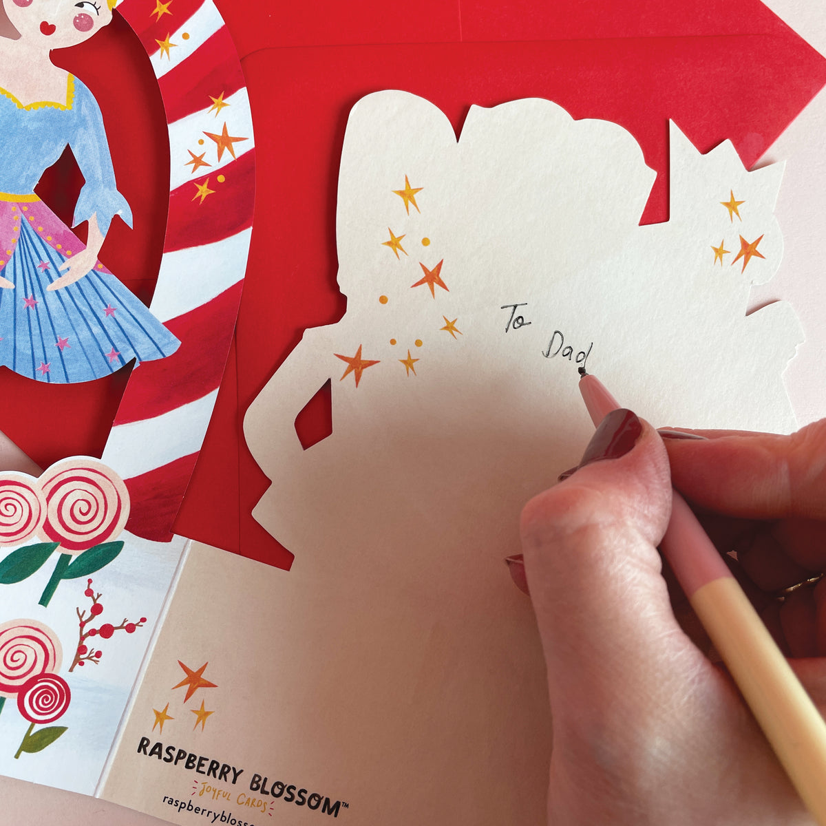 An image of the back of a 3D fold out christmas card and the space to write a message, bring illustrated by a white person with red nail polish.